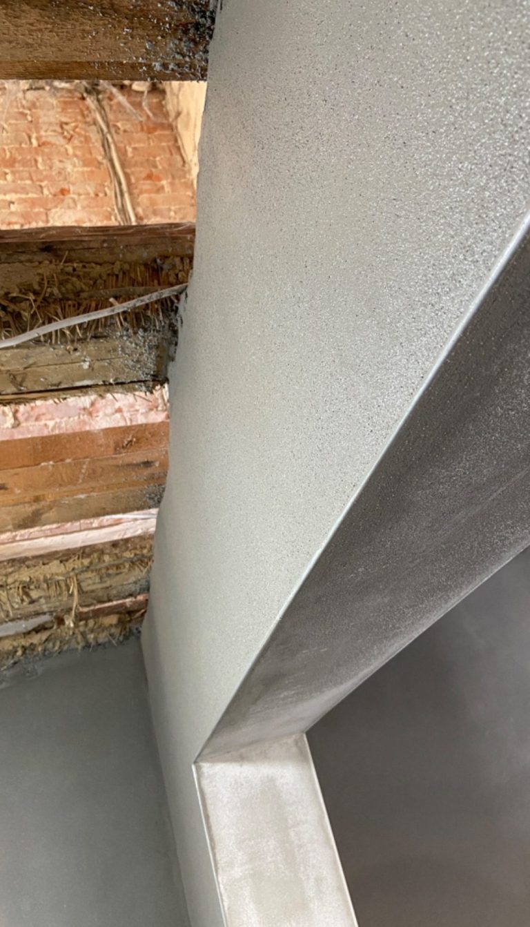 Innenputz Raum mit rohen Holzbalken und glatter, grauer verputzter Wandoberfläche.