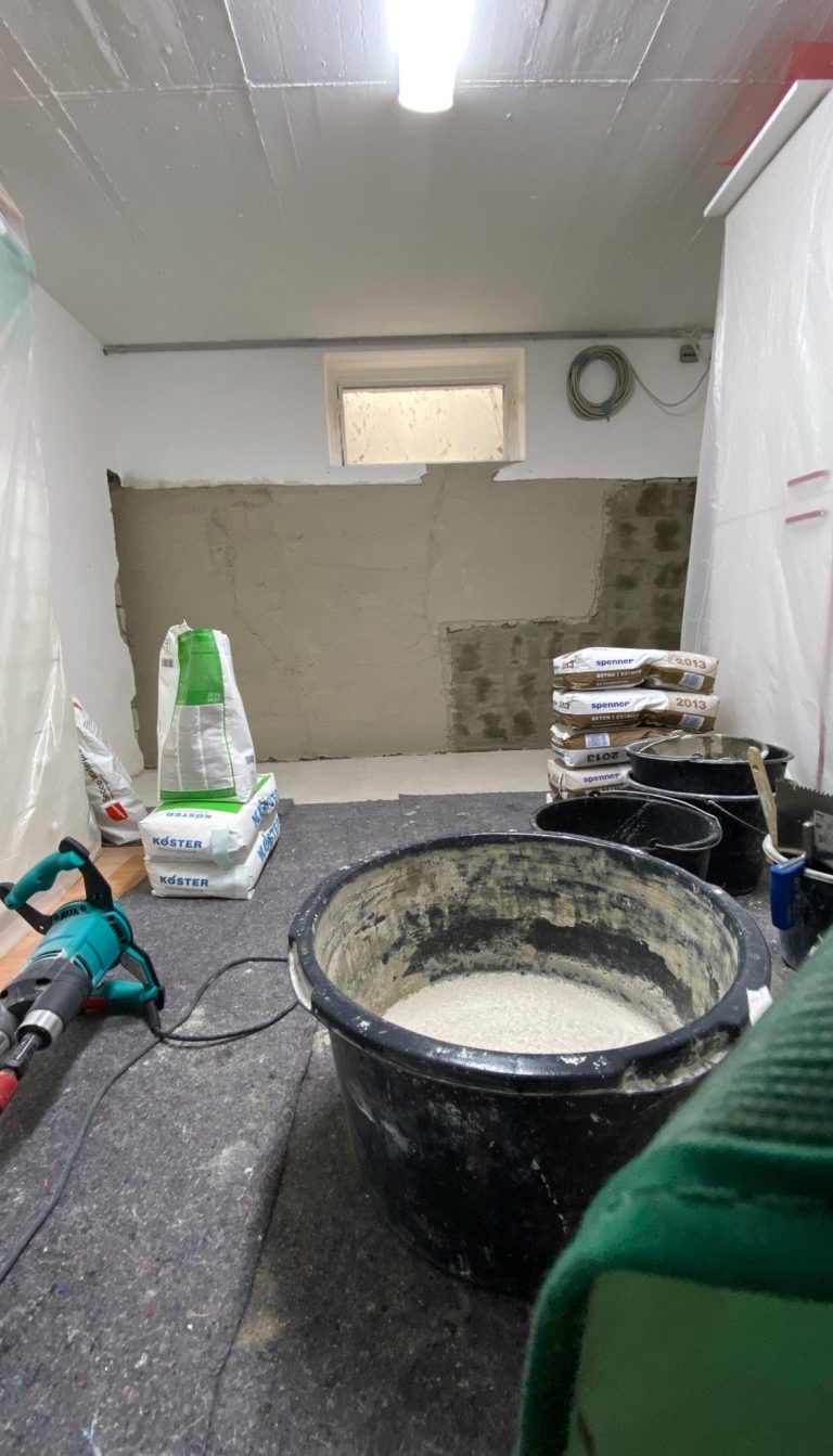 Verputzarbeiten Ein Handwerker trägt schwarzen Mörtel mit einer Kelle auf eine graue Fläche auf.