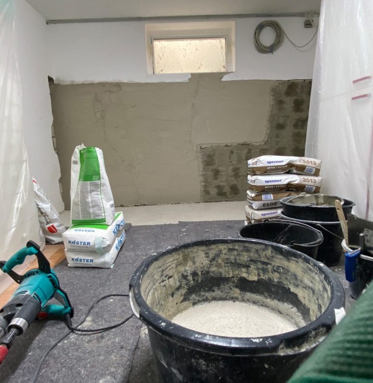 Verputzarbeiten Ein Handwerker trägt schwarzen Mörtel mit einer Kelle auf eine graue Fläche auf.