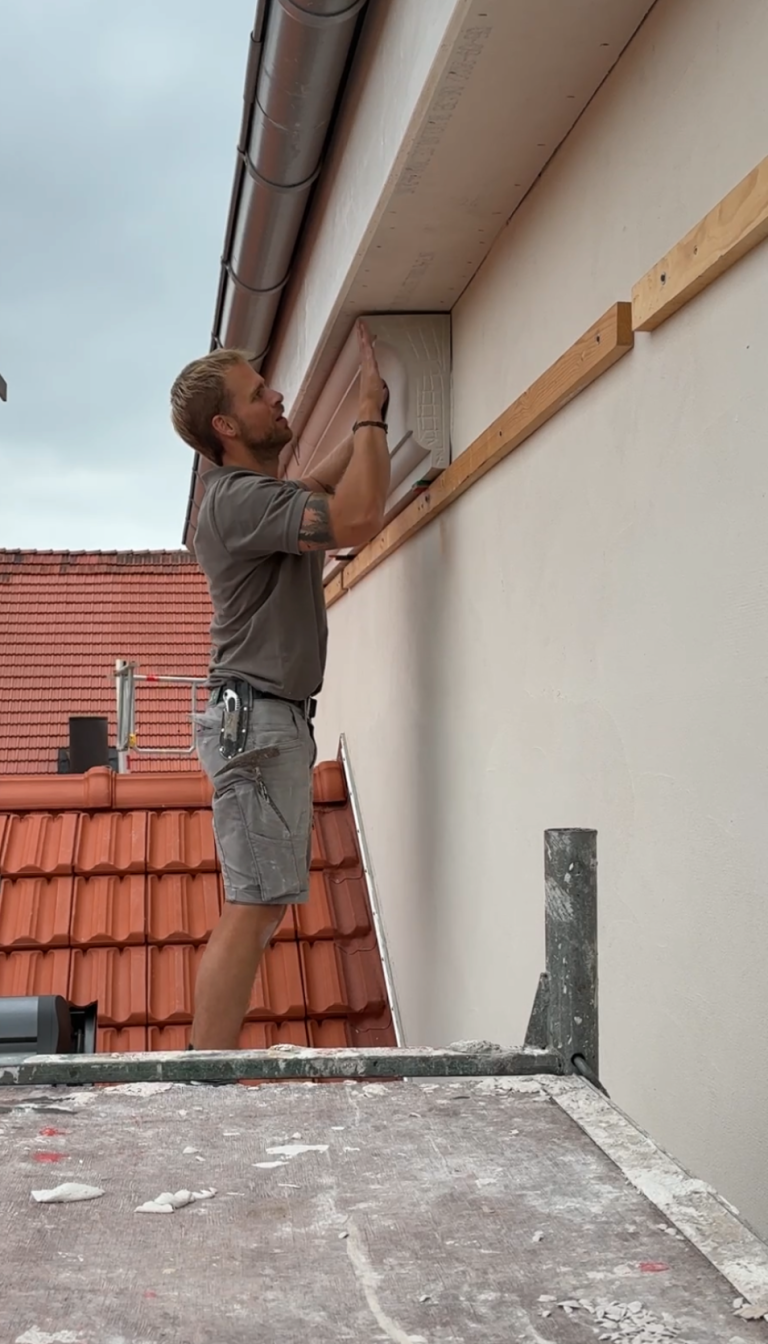 Stuckfassade Fenster mit Bogen und dekorativen Elementen an einer hellen Hausfassade.