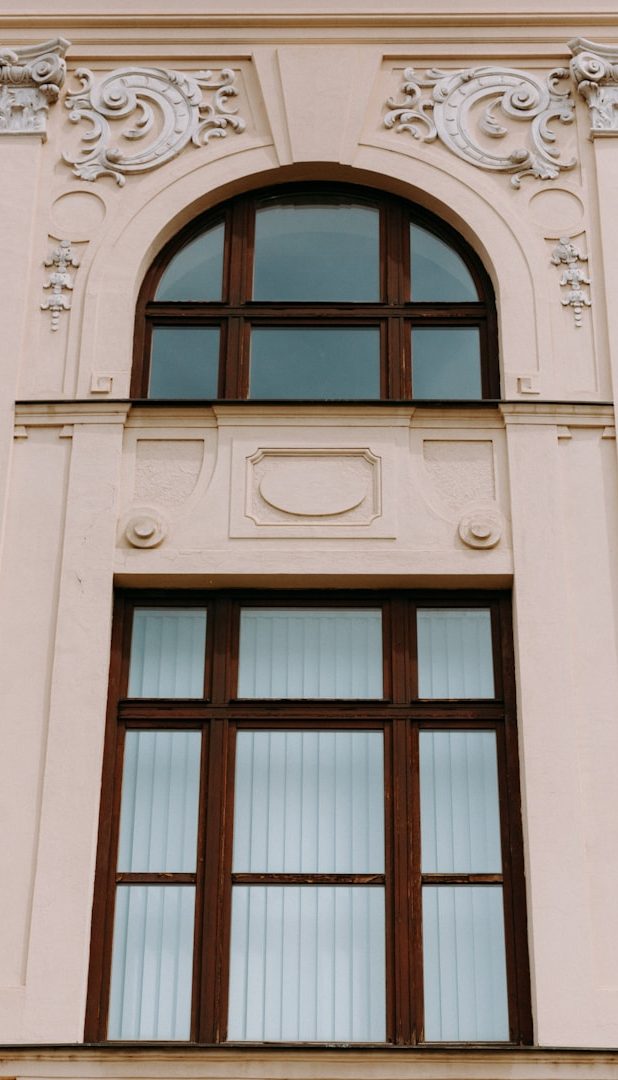 Stuckfassade Fenster mit Bogen und dekorativen Elementen an einer hellen Hausfassade.
